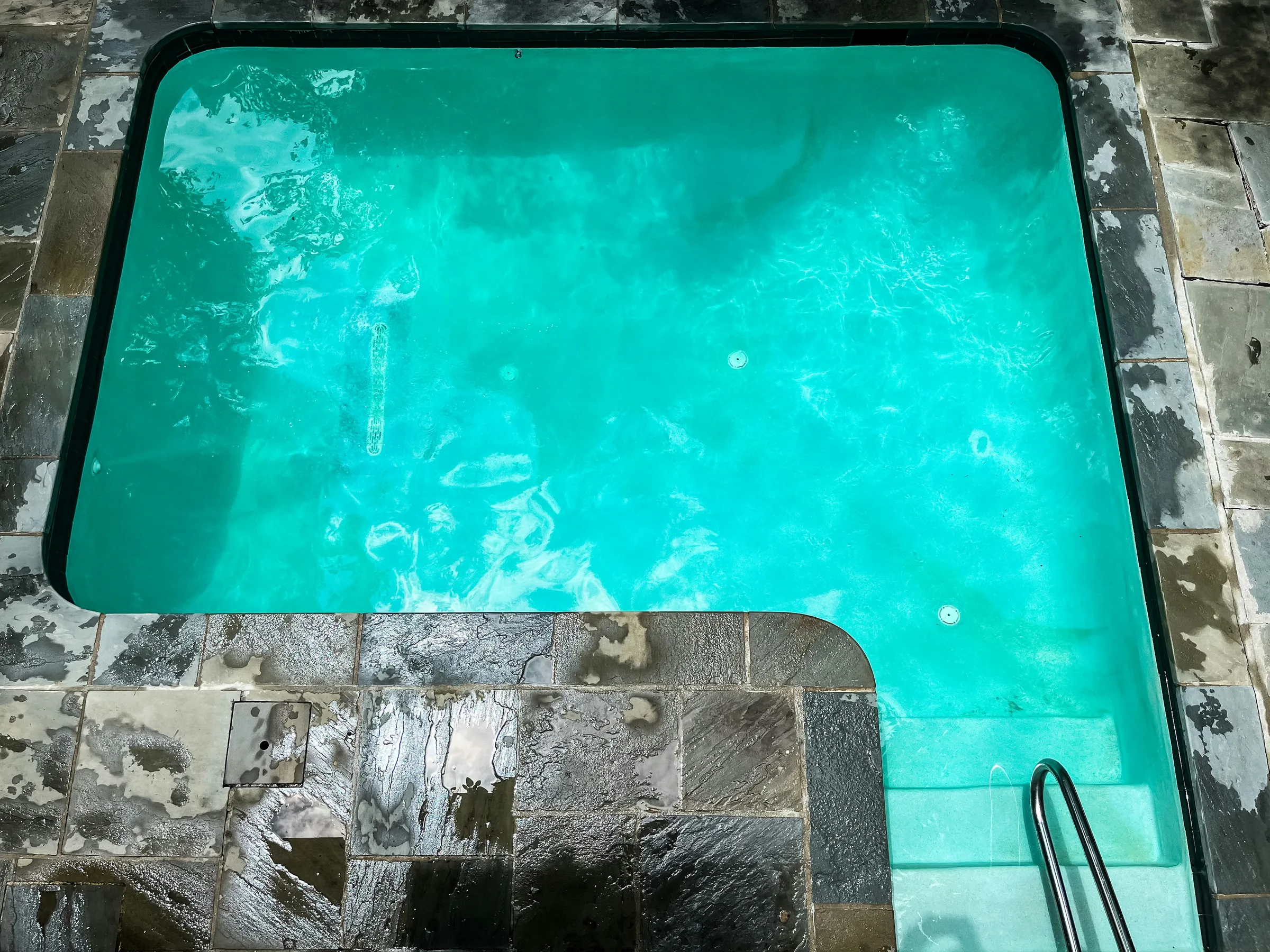 Aerial view of an L-shaped pool and stone patio